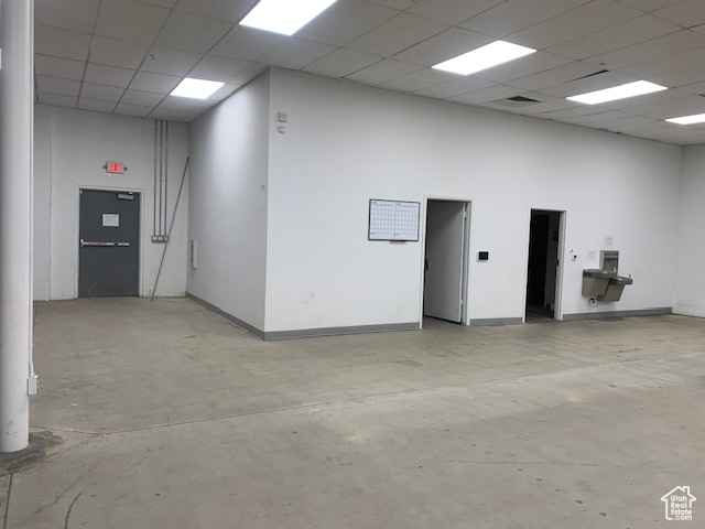 Empty room with concrete flooring, baseboards, a drop ceiling, and a towering ceiling