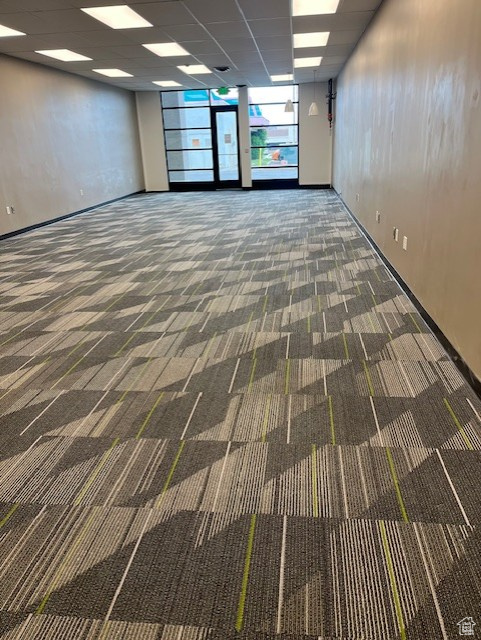 Carpeted empty room featuring a paneled ceiling and baseboards