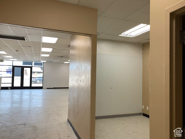 Corridor featuring a drop ceiling, baseboards, and light floors