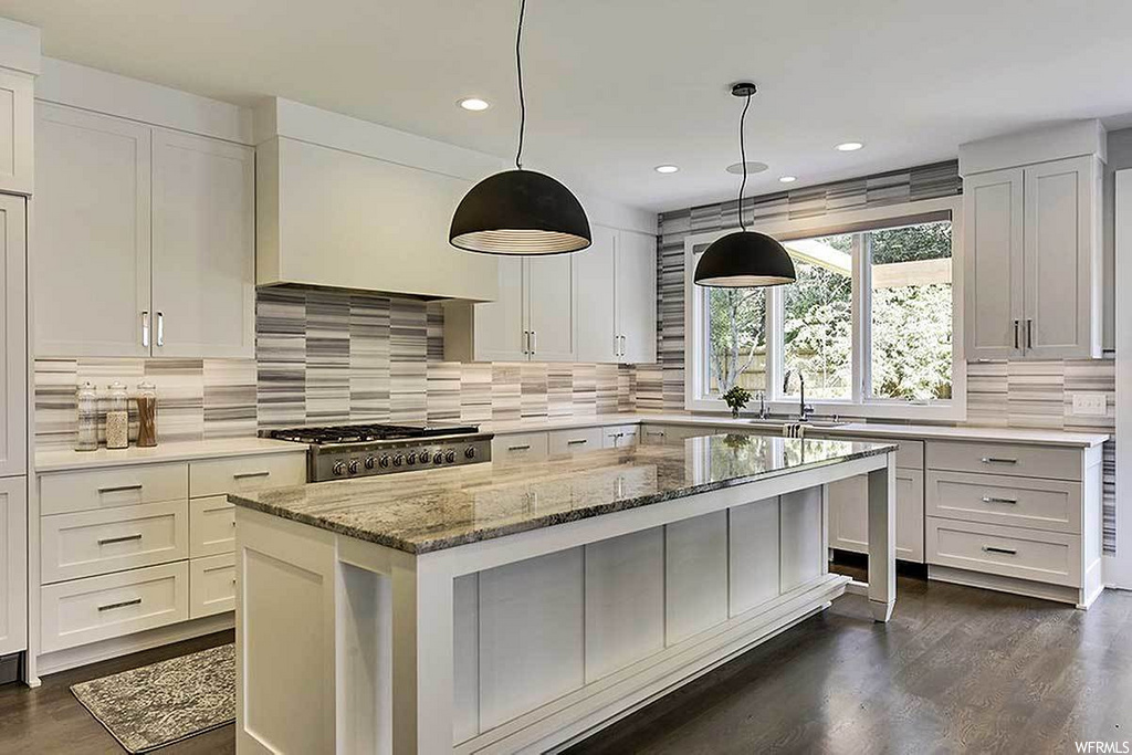 kitchen with a kitchen island, natural light, stainless steel finishes, gas cooktop, dark hardwood floors, white cabinetry, pendant lighting, and light granite-like countertops