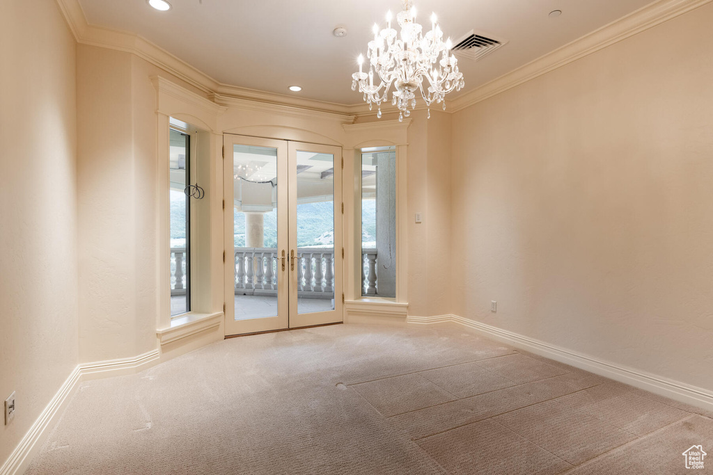 Unfurnished room with light colored carpet, french doors, crown molding, and an inviting chandelier
