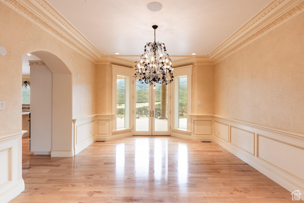 Empty room with an inviting chandelier, ornamental molding, light hardwood / wood-style floors, and french doors