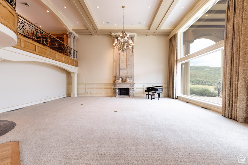 Unfurnished living room with decorative columns, light carpet, a chandelier, a mountain view, and beam ceiling