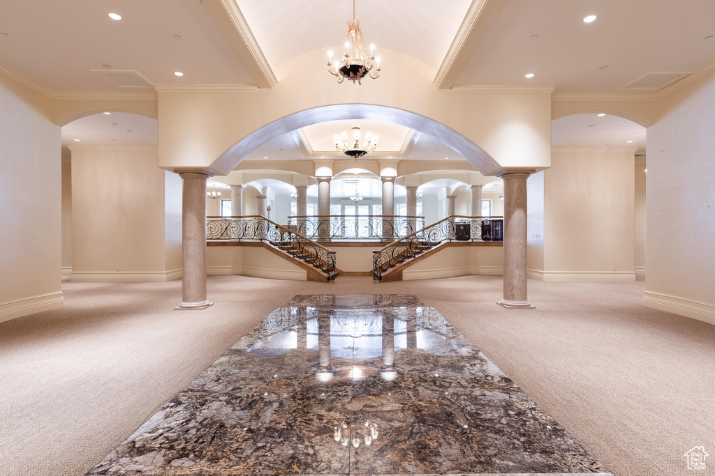 Carpeted foyer with a chandelier, ornamental molding, and ornate columns