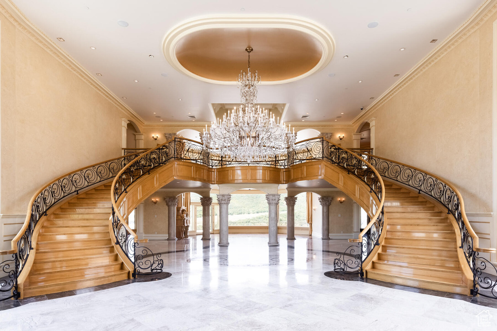 Stairway featuring a notable chandelier, a towering ceiling, light tile floors, and ornate columns