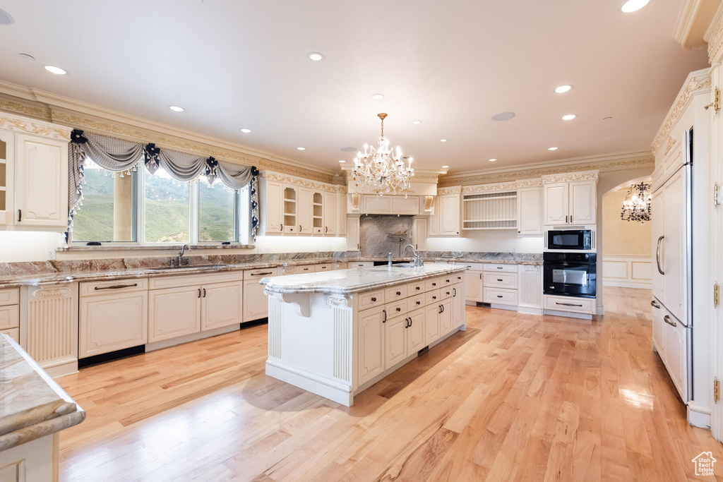 Kitchen with a center island with sink, black appliances, an inviting chandelier, light wood-type flooring, and light stone counters