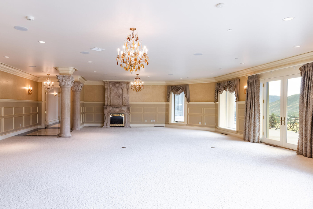 Unfurnished living room with an inviting chandelier, a fireplace, light carpet, and decorative columns