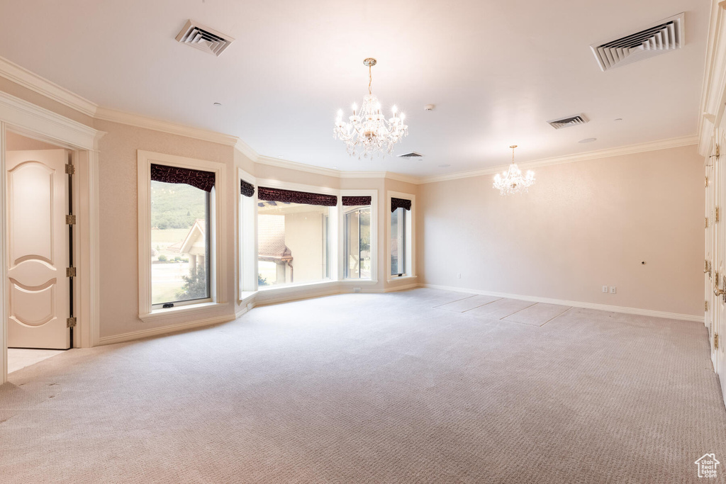 Empty room featuring a notable chandelier, light carpet, and crown molding