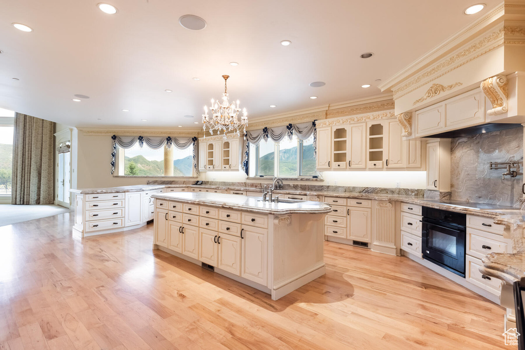 Kitchen featuring a chandelier, oven, plenty of natural light, and a center island with sink