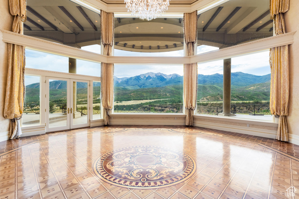 Unfurnished sunroom featuring an inviting chandelier, a mountain view, french doors, and lofted ceiling with beams