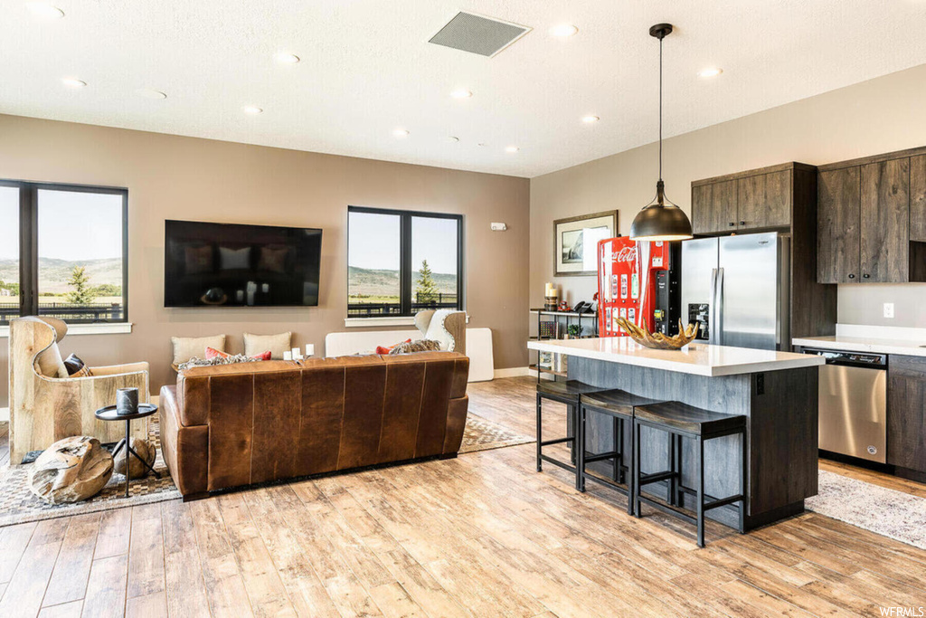 Kitchen featuring a breakfast bar area, a wealth of natural light, stainless steel dishwasher, TV, refrigerator, light countertops, pendant lighting, dark brown cabinetry, and light parquet floors