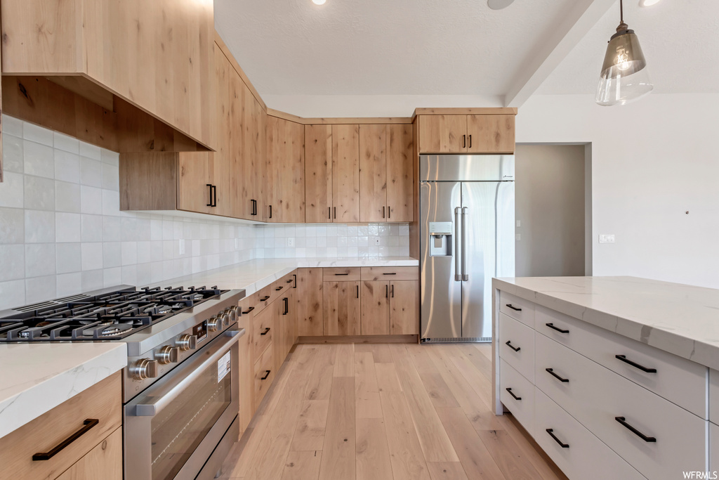 Kitchen featuring light hardwood / wood-style flooring, light stone countertops, premium appliances, tasteful backsplash, and decorative light fixtures