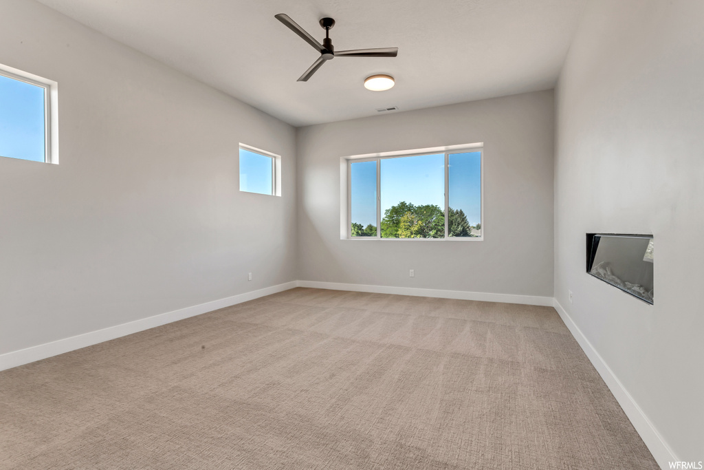 Carpeted empty room with ceiling fan and a wealth of natural light