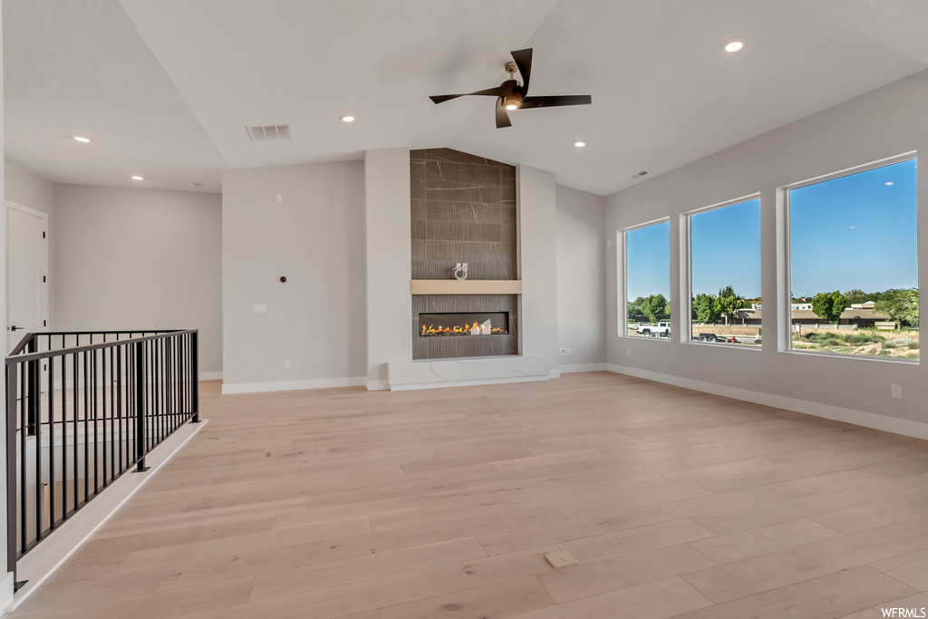 Unfurnished living room with built in features, light hardwood / wood-style flooring, a tiled fireplace, ceiling fan, and lofted ceiling