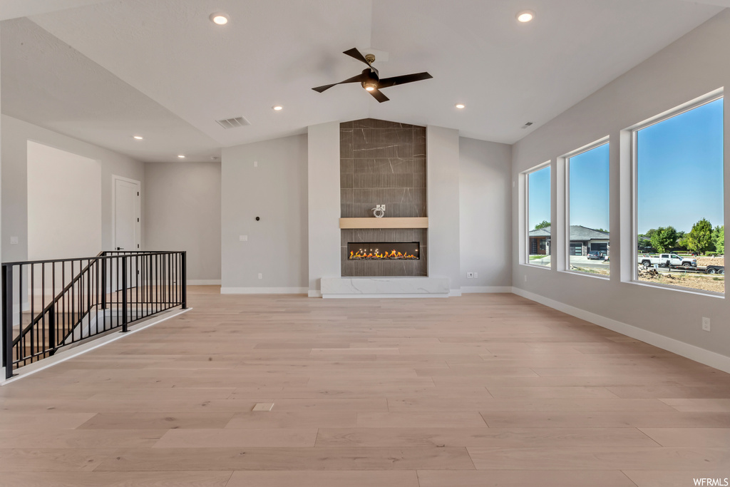 Unfurnished living room with built in features, a tile fireplace, ceiling fan, and light wood-type flooring