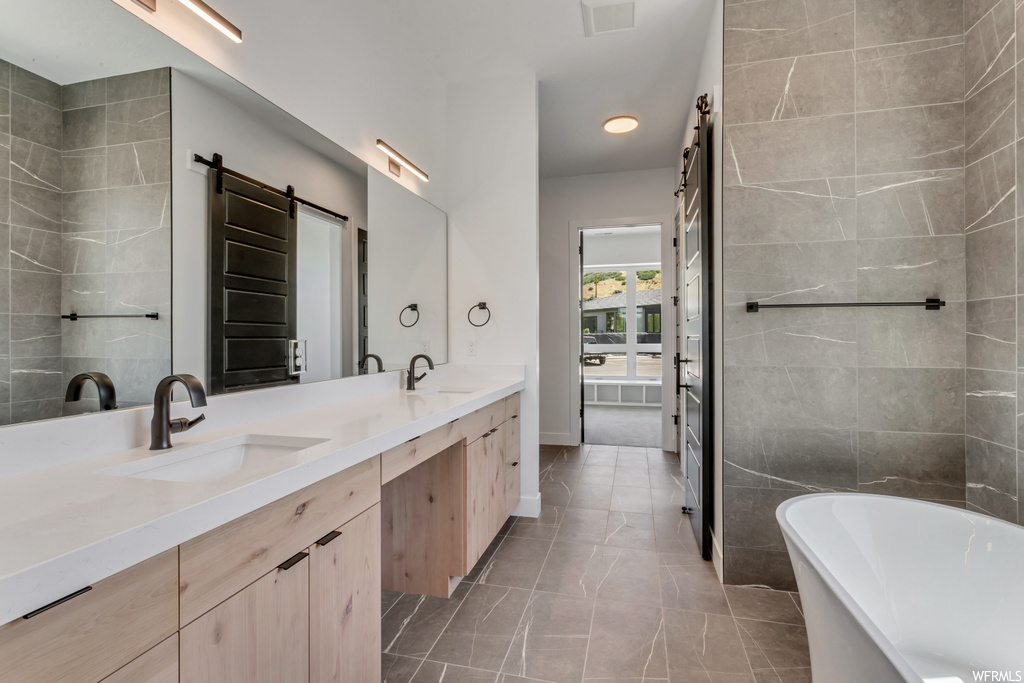 Bathroom with tile floors, tile walls, a bath to relax in, and dual bowl vanity