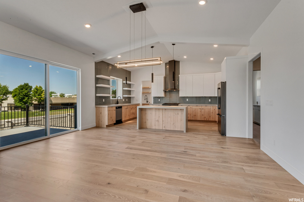 Kitchen featuring hanging light fixtures, appliances with stainless steel finishes, vaulted ceiling, tasteful backsplash, and light hardwood / wood-style flooring