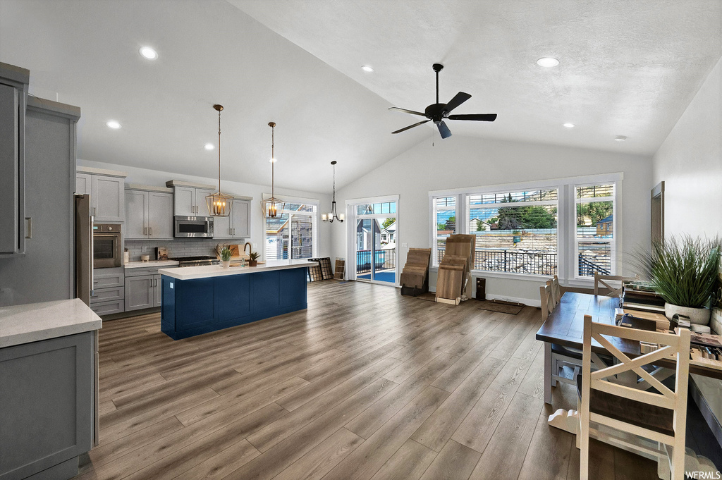 kitchen featuring a kitchen island, natural light, vaulted ceiling, oven, stainless steel microwave, pendant lighting, light countertops, and light hardwood flooring