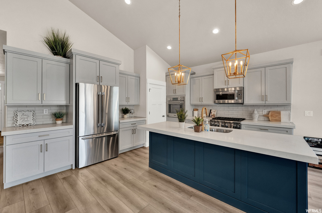 kitchen featuring lofted ceiling, oven, refrigerator, gas stovetop, microwave, light parquet floors, white cabinetry, light countertops, and pendant lighting