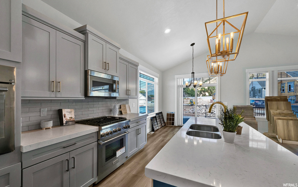 kitchen featuring natural light, vaulted ceiling, wood-type flooring, gas range oven, microwave, light countertops, white cabinetry, and pendant lighting
