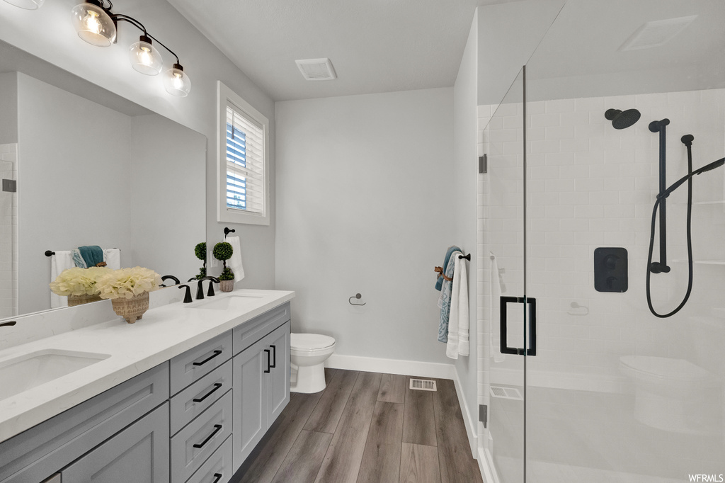 full bathroom featuring natural light, hardwood flooring, dual vanity, mirror, shower cabin, and toilet