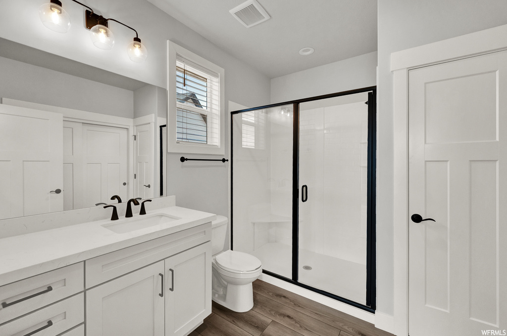 full bathroom with wood-type flooring, natural light, shower with shower door, mirror, toilet, and vanity
