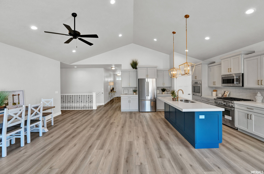 kitchen featuring lofted ceiling, a kitchen island, oven, microwave, refrigerator, gas range oven, light hardwood floors, light countertops, pendant lighting, and white cabinets