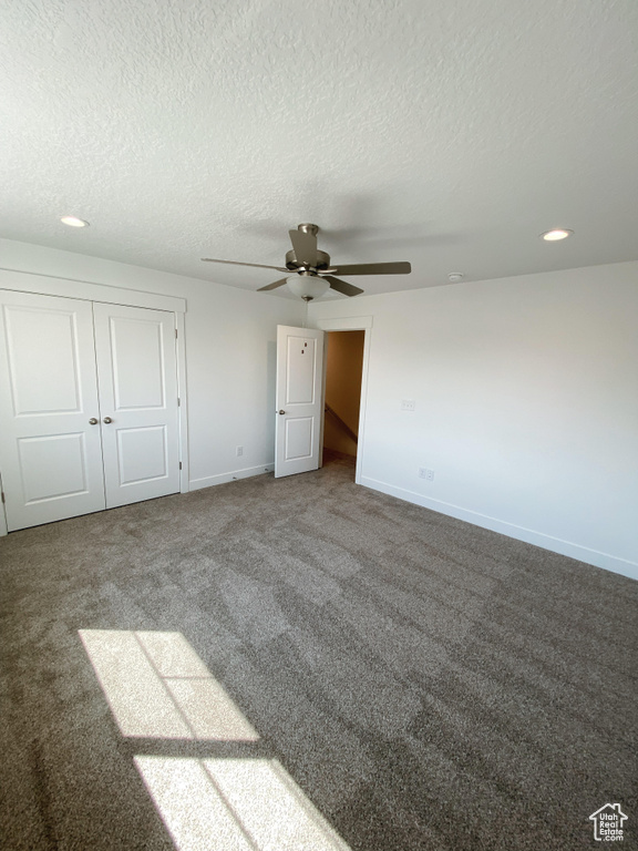 Unfurnished bedroom with dark carpet, a textured ceiling, ceiling fan, and a closet