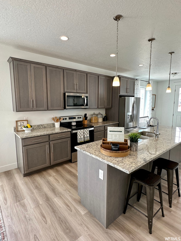 kitchen with a center island, stainless steel refrigerator, microwave, range oven, light parquet floors, pendant lighting, light stone countertops, and dark brown cabinetry