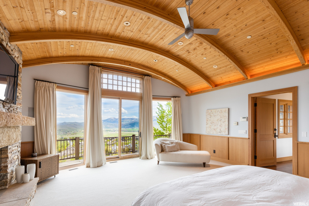 carpeted bedroom featuring lofted ceiling with beams, a ceiling fan, a fireplace, and multiple windows