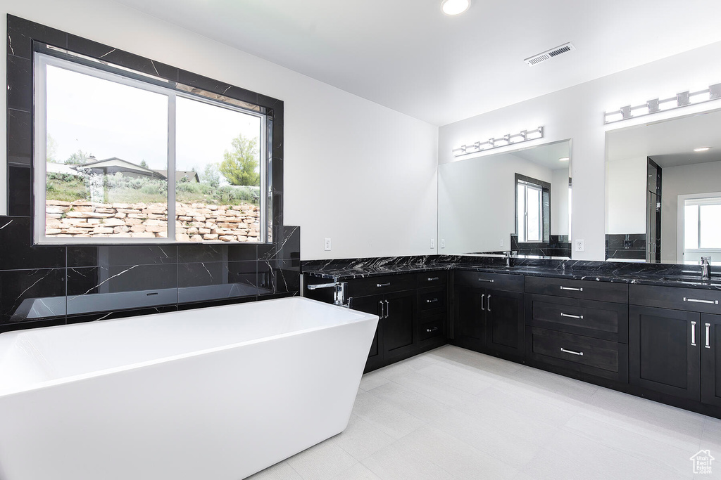 Bathroom featuring a healthy amount of sunlight, tile flooring, dual sinks, and vanity with extensive cabinet space