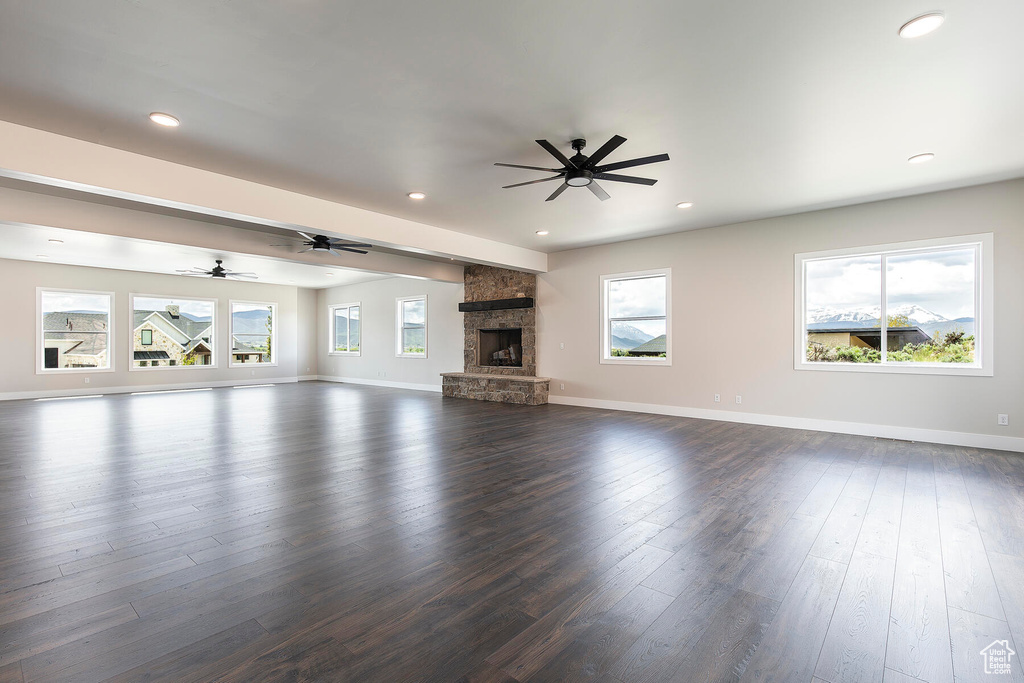 Unfurnished living room featuring a stone fireplace, ceiling fan, and dark hardwood / wood-style flooring