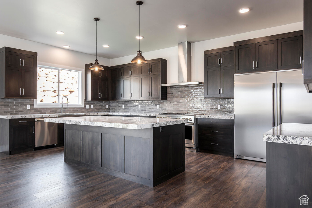 Kitchen with wall chimney range hood, dark hardwood / wood-style floors, tasteful backsplash, high end appliances, and pendant lighting