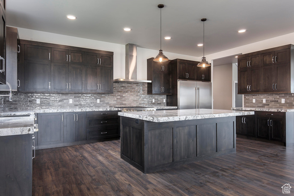 Kitchen featuring backsplash, a kitchen island, wall chimney range hood, and appliances with stainless steel finishes