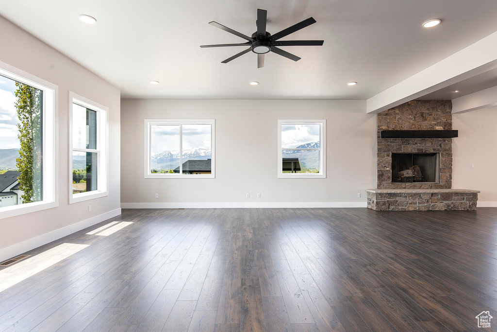 Unfurnished living room featuring dark hardwood / wood-style floors, a stone fireplace, and ceiling fan