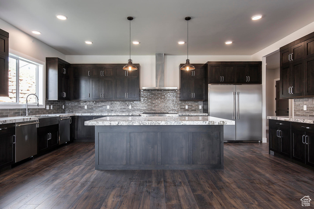 Kitchen featuring wall chimney range hood, dark hardwood / wood-style flooring, a kitchen island, and appliances with stainless steel finishes