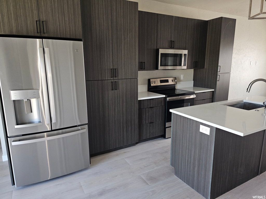 Kitchen with light parquet floors, dark brown cabinetry, appliances with stainless steel finishes, and light countertops