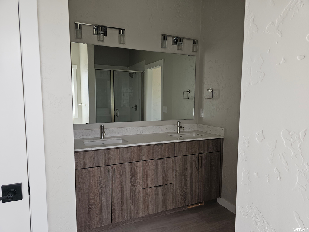 Bathroom featuring double sink vanity, an enclosed shower, mirror, and dark hardwood floors