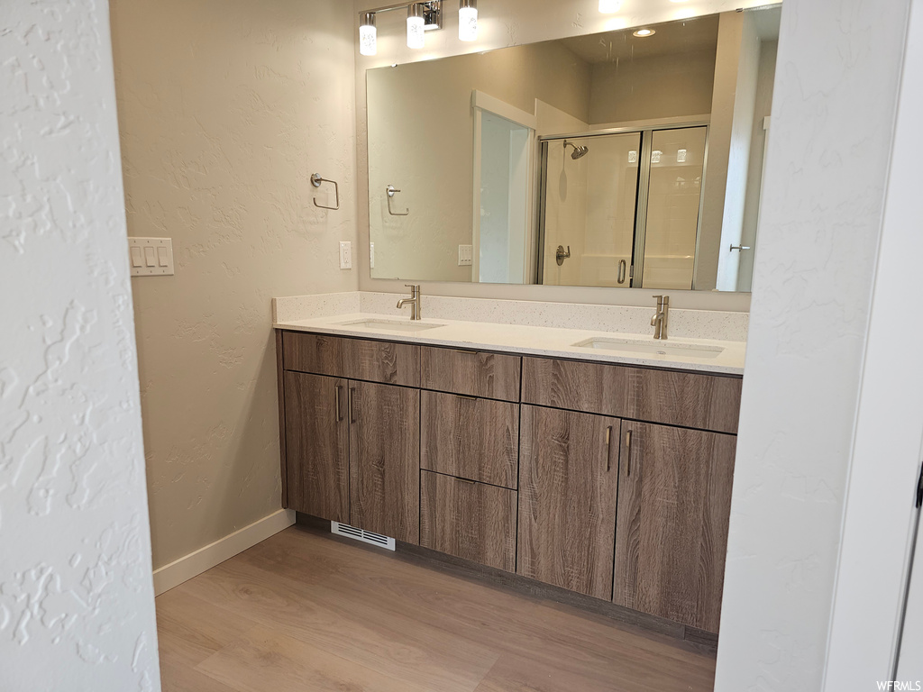 Bathroom with an enclosed shower, light hardwood floors, mirror, and dual bowl vanity