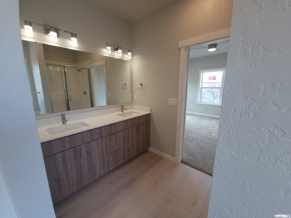 Bathroom with hardwood floors, natural light, shower booth, double sink vanity, and mirror