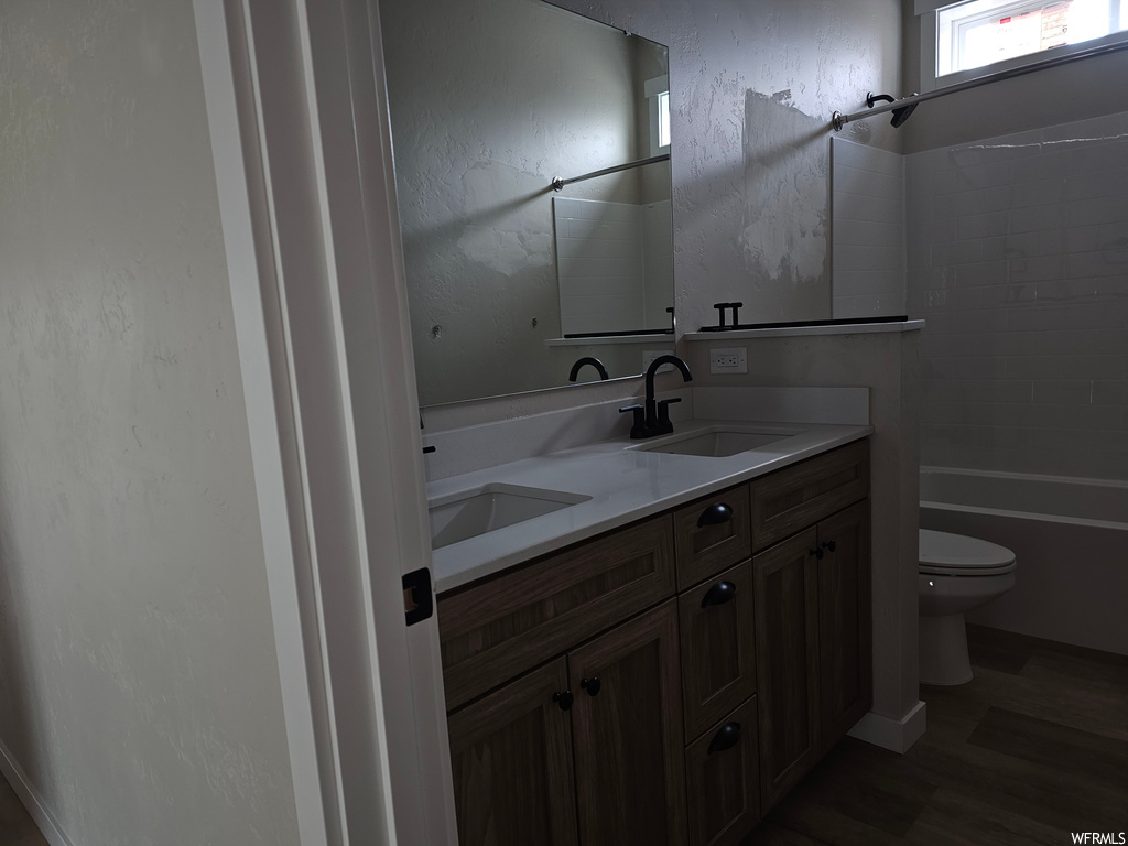 Full bathroom with dark hardwood flooring, shower / washtub combination, double sink vanity, and mirror