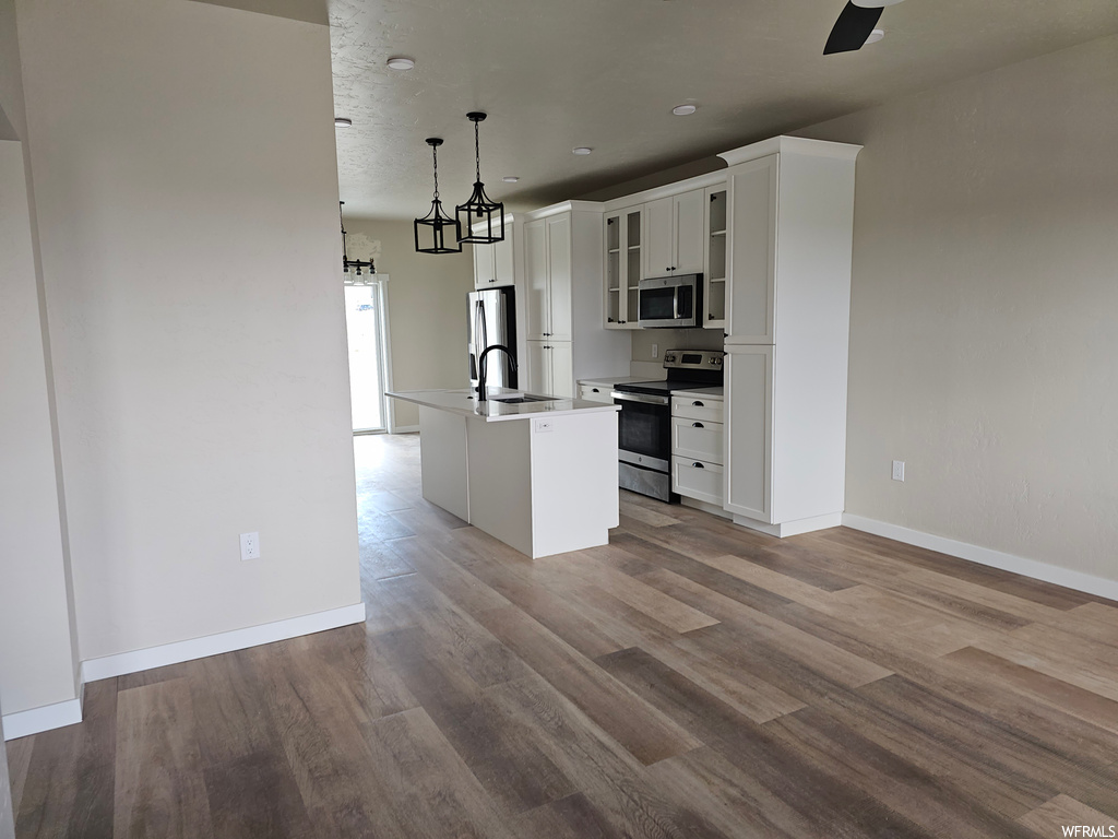 Kitchen featuring dark hardwood flooring, appliances with stainless steel finishes, white cabinets, and pendant lighting