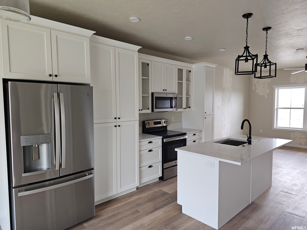 Kitchen with appliances with stainless steel finishes, wood-type flooring, white cabinets, and hanging light fixtures
