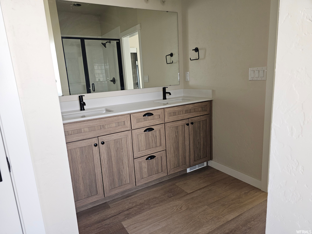 Bathroom with an enclosed shower, dual bowl vanity, mirror, and dark hardwood floors