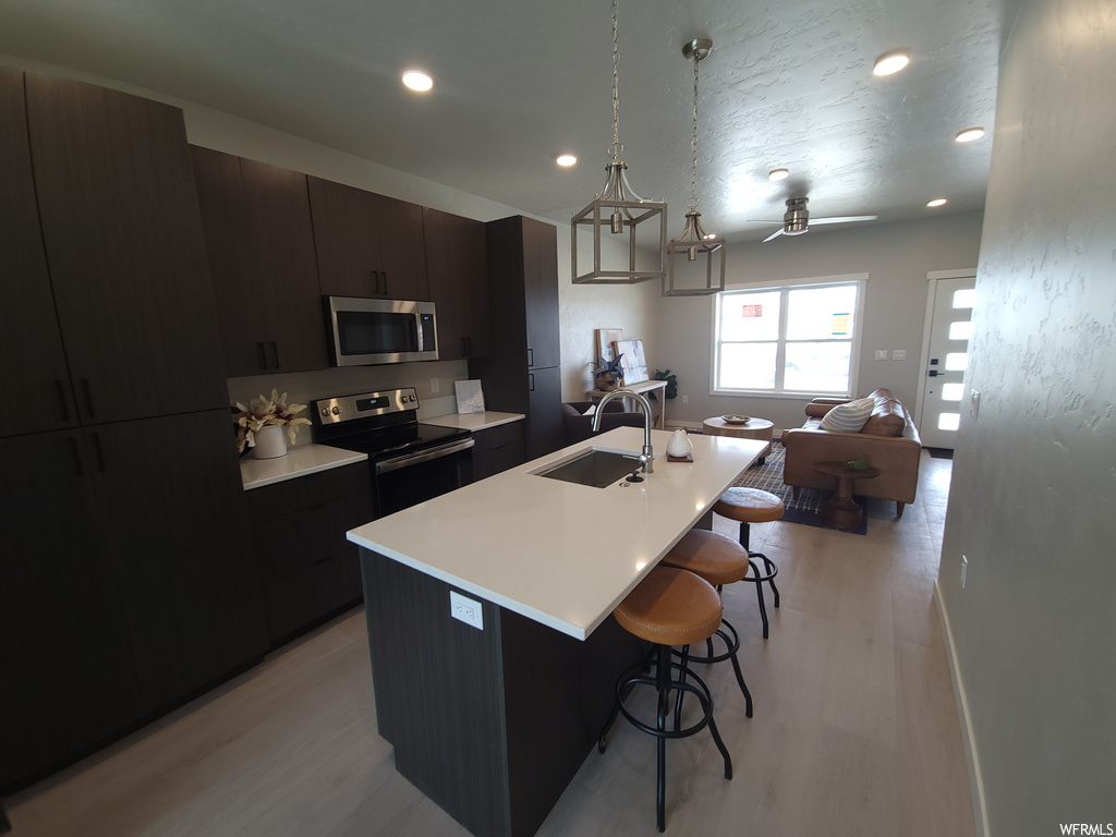 Kitchen featuring a breakfast bar, natural light, a kitchen island, microwave, range oven, dark brown cabinets, light countertops, and light parquet floors