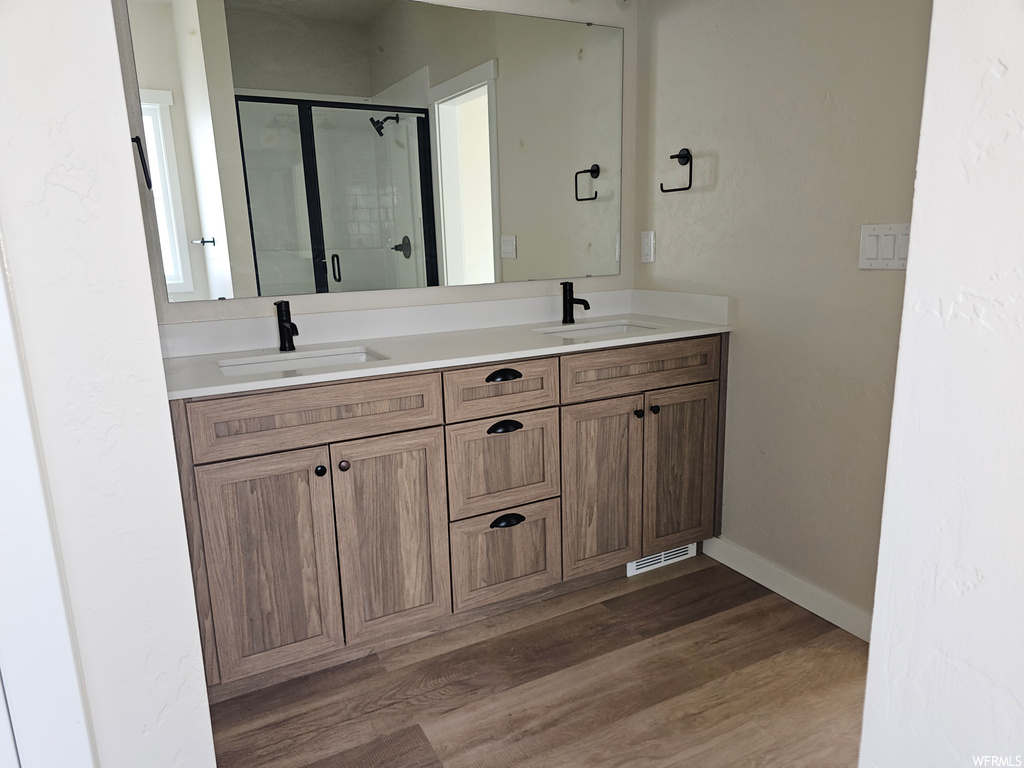 Bathroom with an enclosed shower, light hardwood flooring, double sink vanity, and mirror