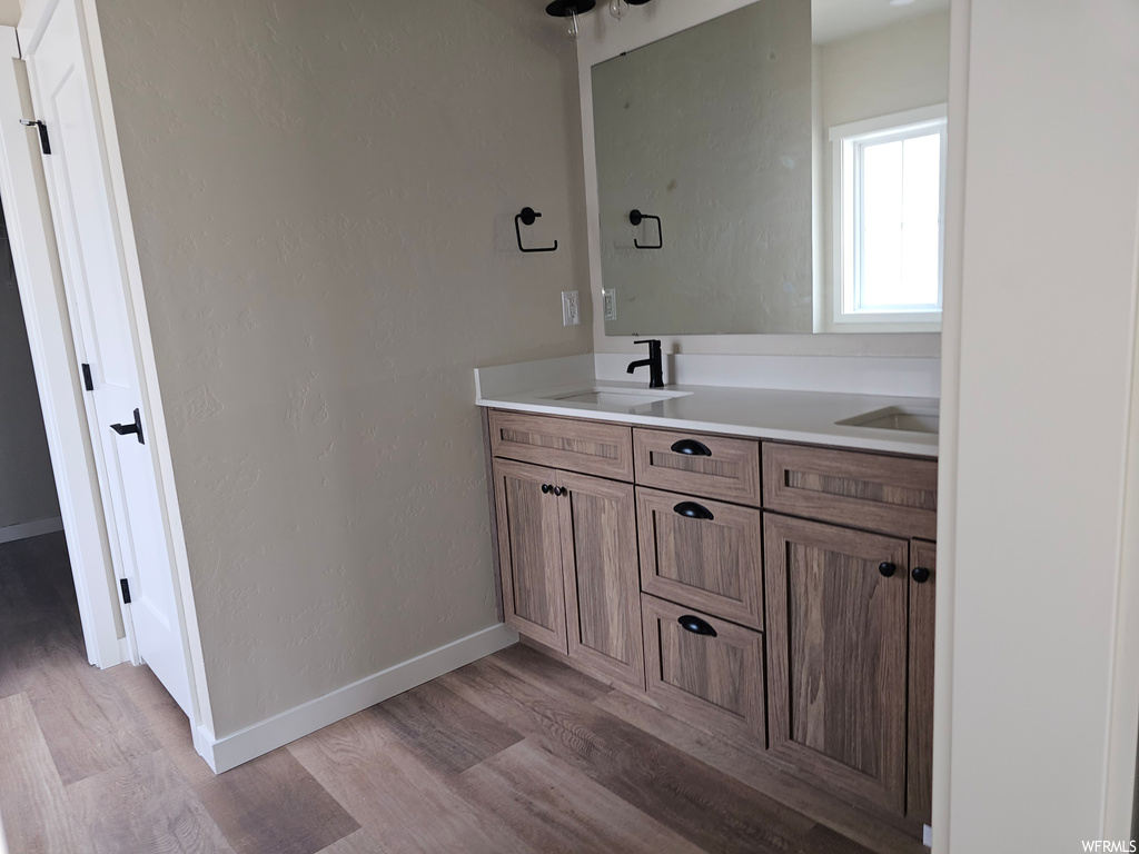 Bathroom featuring double sink vanity, light hardwood floors, and mirror