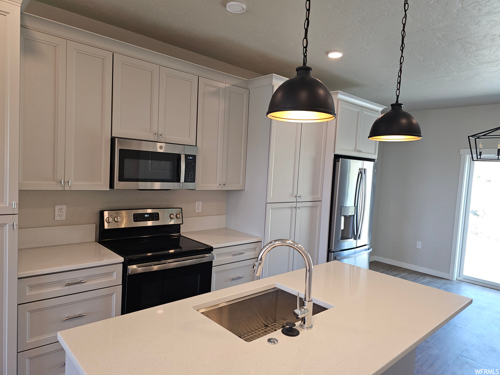 Kitchen with white cabinets, light countertops, wood-type flooring, hanging light fixtures, and appliances with stainless steel finishes