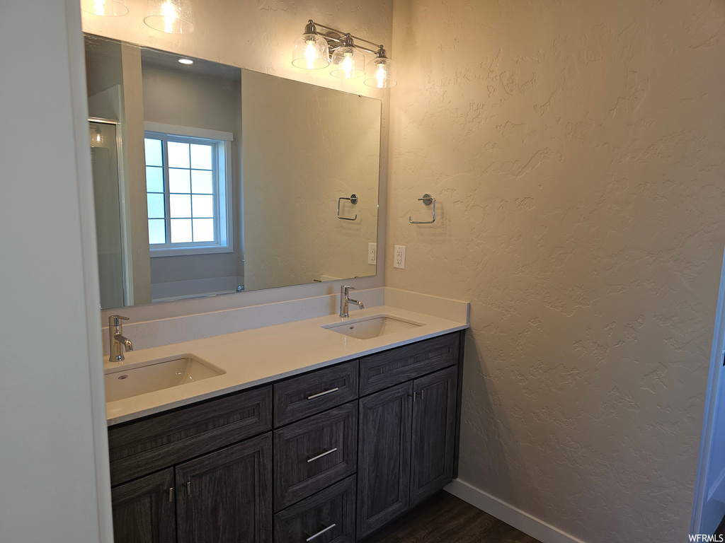 Bathroom featuring dual vanity, mirror, and dark hardwood floors