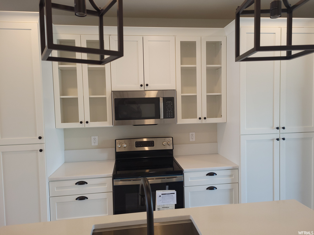 Kitchen featuring electric range oven, microwave, light countertops, and white cabinetry